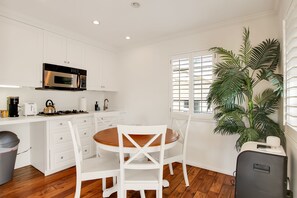 Una cocina moderna con armarios blancos, microondas integrado y comedor con mesa de madera y sillas blancas.