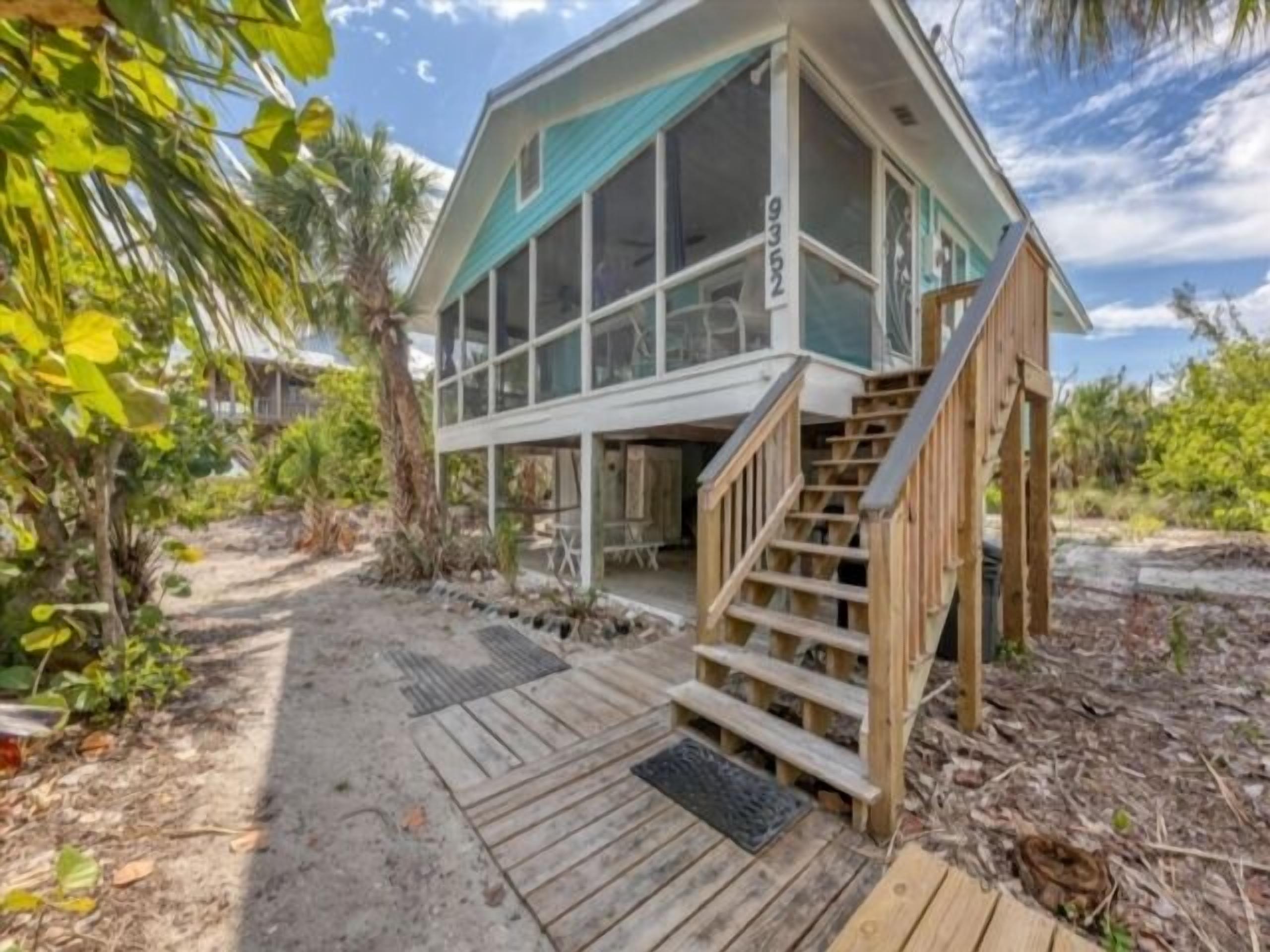 Une maison de plage à deux étages, dotée d’une terrasse en bois et d’un escalier menant à l’étage supérieur.