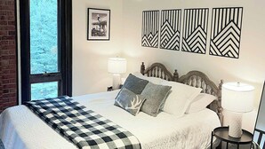 Une chambre avec un grand lit, deux lampes de chevet, une fenêtre donnant sur un beau paysage et des œuvres d’art murales.