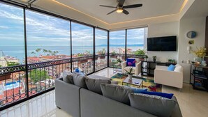 Een moderne woonkamer met een groot balkon, een plafondventilator en een aan de muur bevestigde televisie.