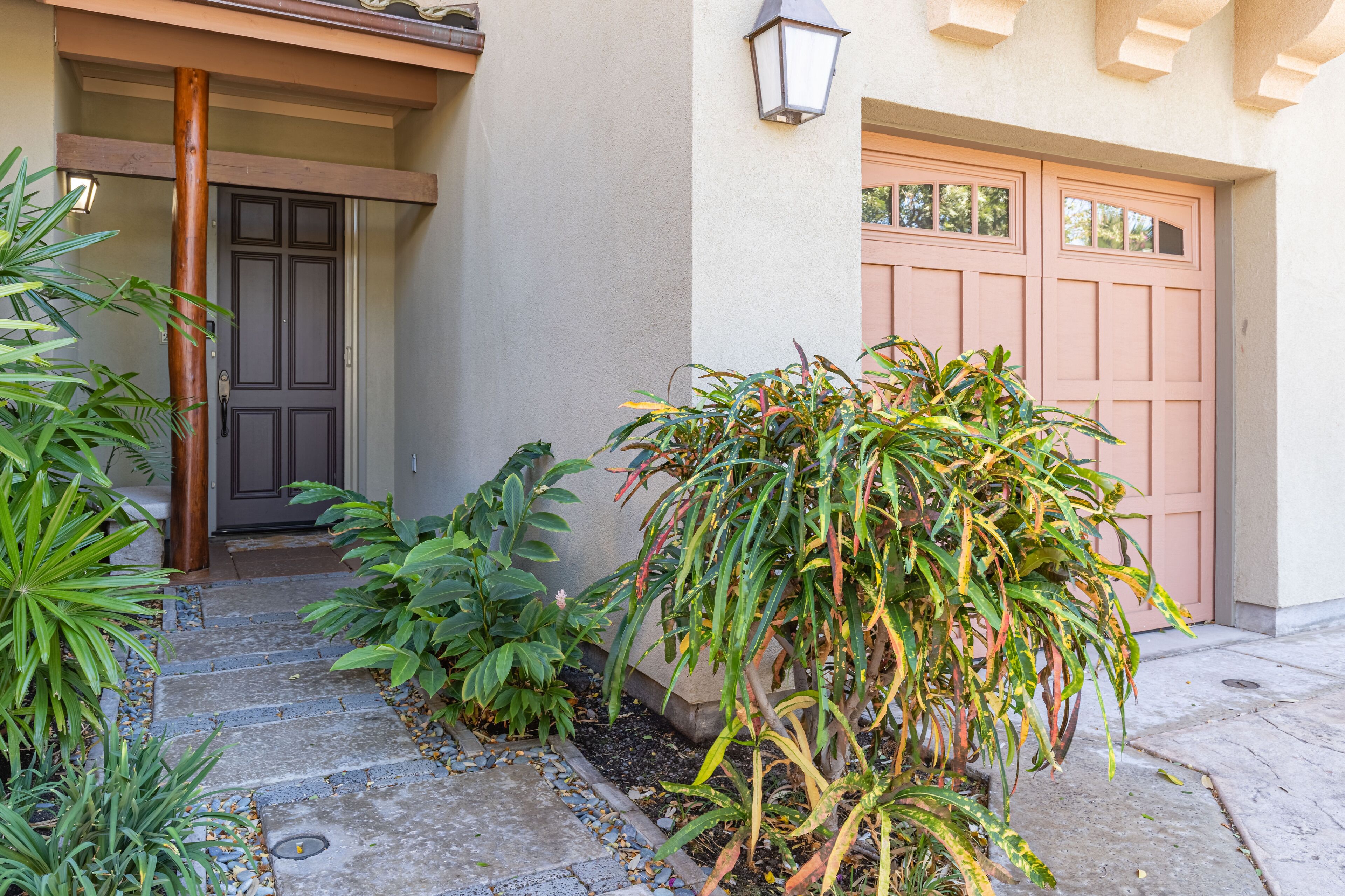 Une maison avec une porte d’entrée, un garage et un jardin bien entretenu où poussent différentes espèces de plantes.