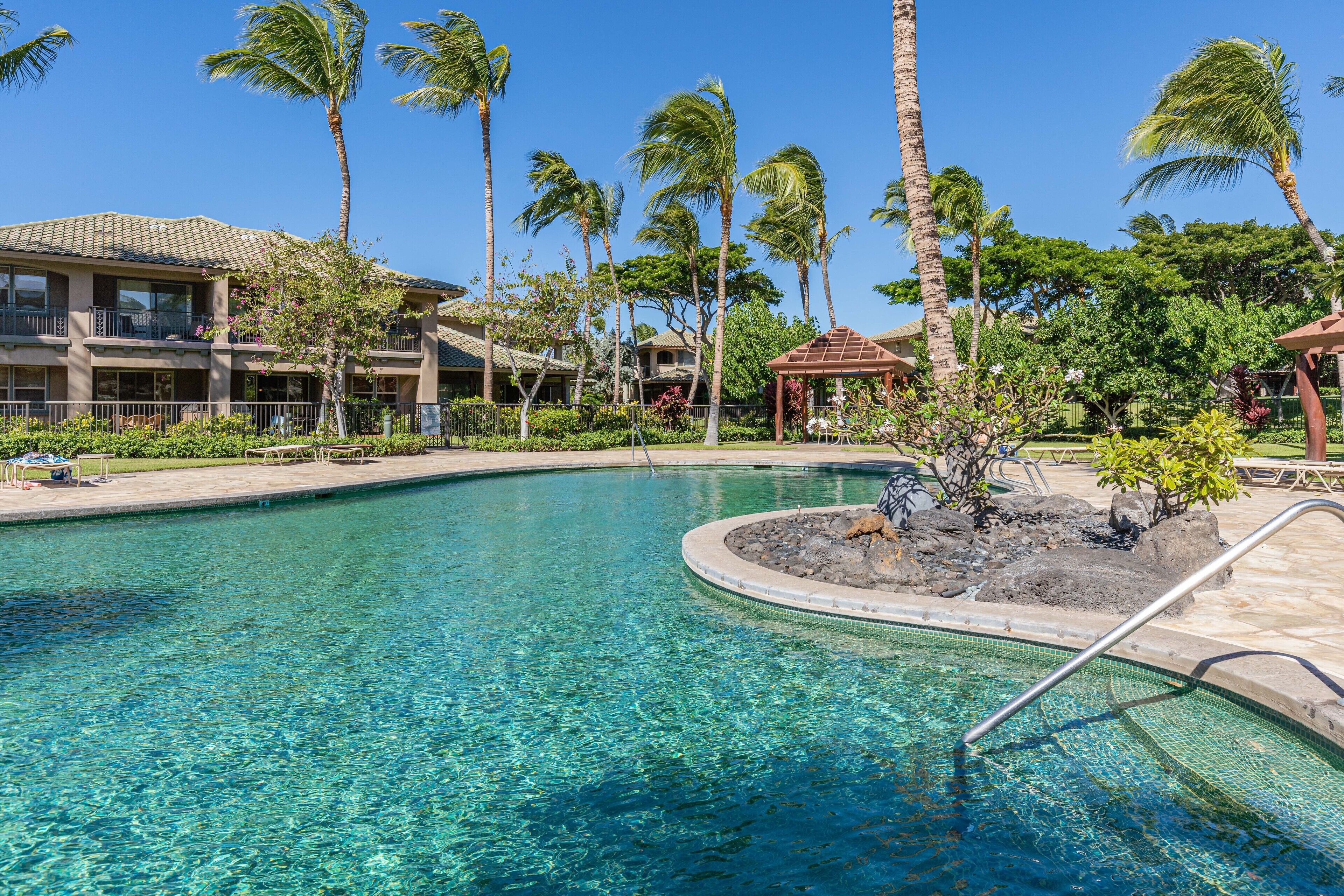 A clear pool with a palm tree and a gazebo in the center.
