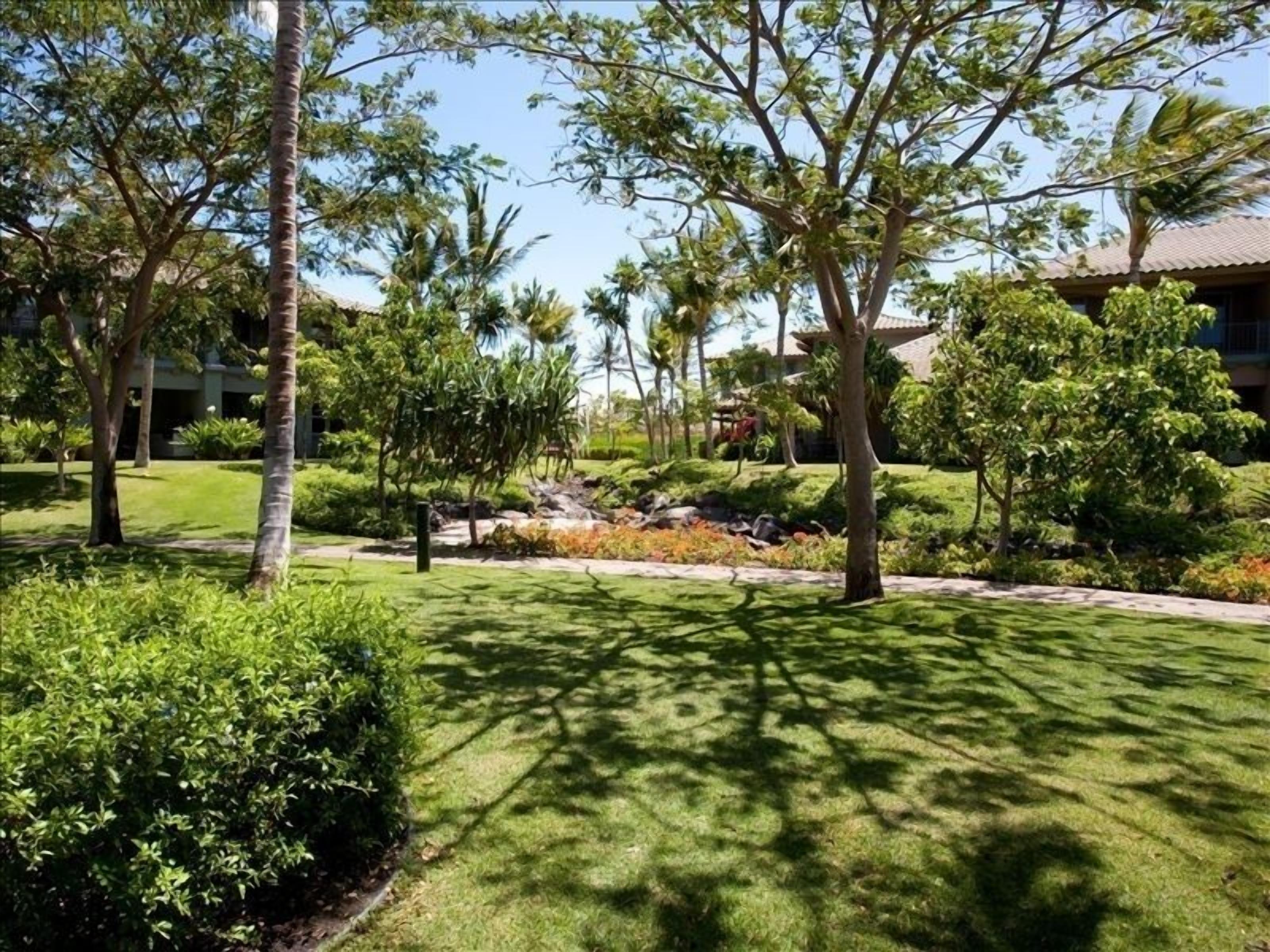 Un jardin bien entretenu, agrémenté de divers arbres et arbustes, d’un petit élément décoratif aquatique et d’un bâtiment en arrière-plan.