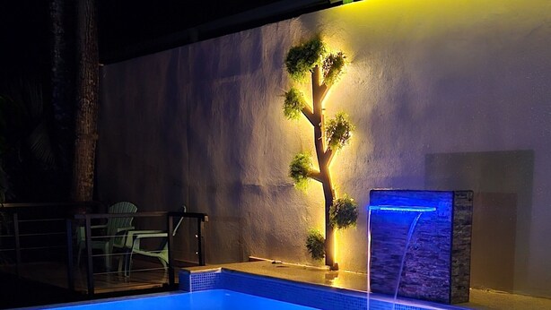 A swimming pool with a waterfall feature, surrounded by a low wall and potted plants.