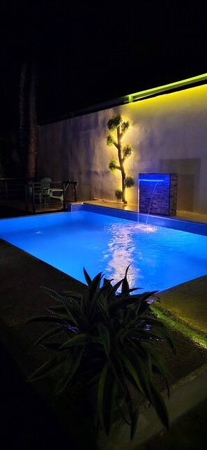 A swimming pool with a waterfall feature, surrounded by a low wall and potted plants.