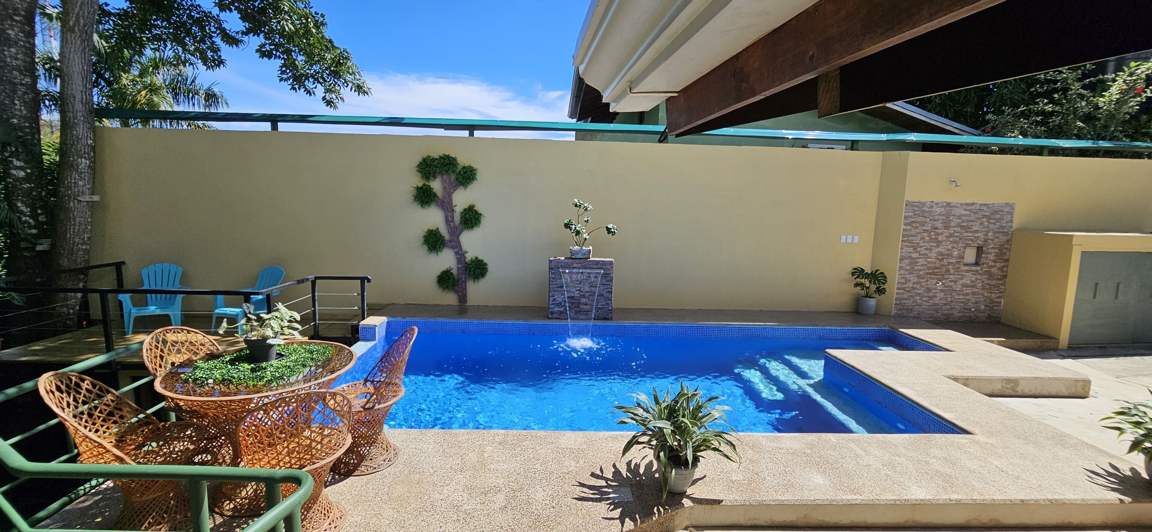 Ein Swimmingpool mit blauem Mosaikrand, umgeben von Korbstühlen und Topfpflanzen.