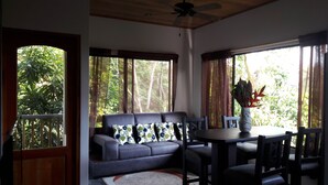 A room with a sofa, dining table, chairs, and a ceiling fan.