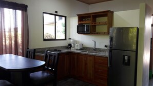 A compact kitchen with wooden cabinets, a stainless steel refrigerator, a microwave, a coffee maker, and a toaster.