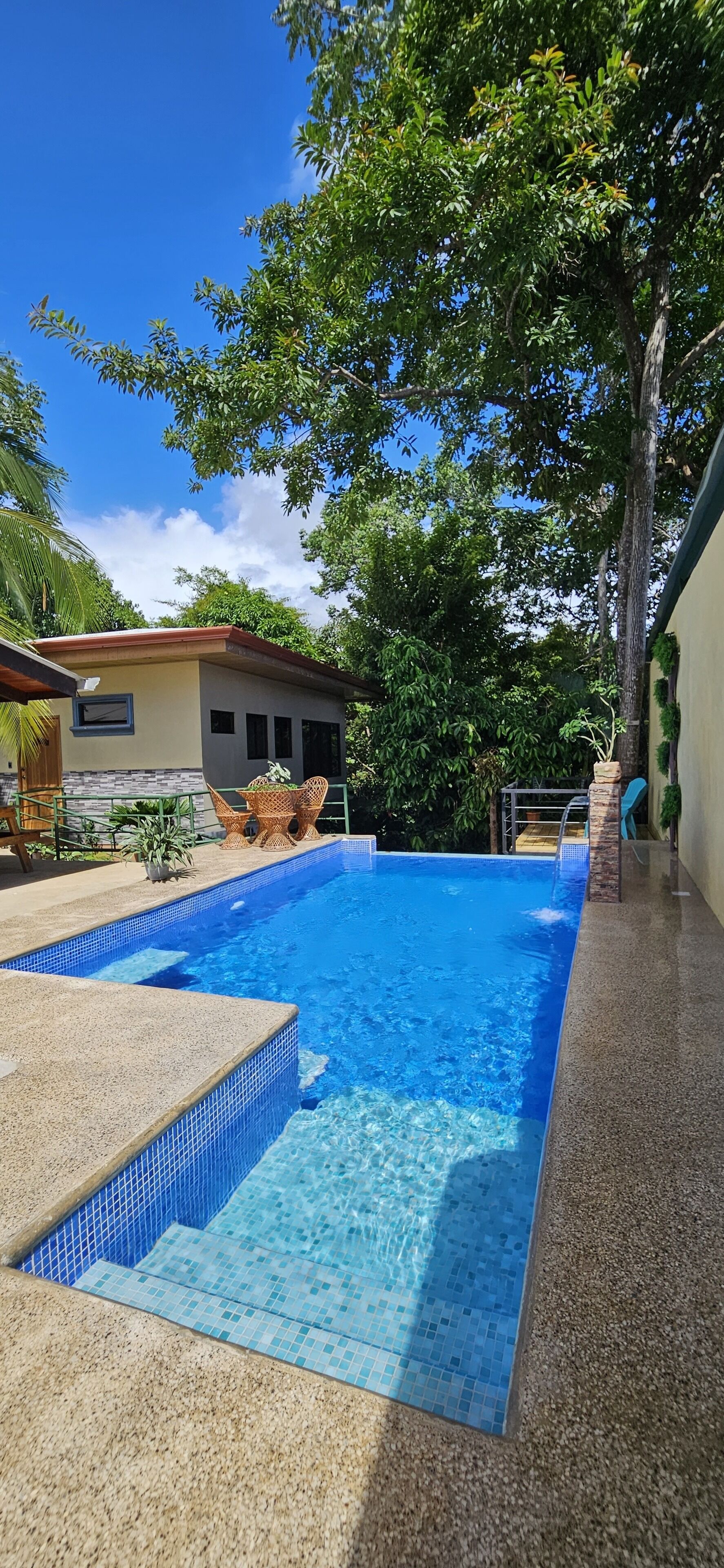 A swimming pool with tiled edges, surrounded by a patio area with outdoor furniture.