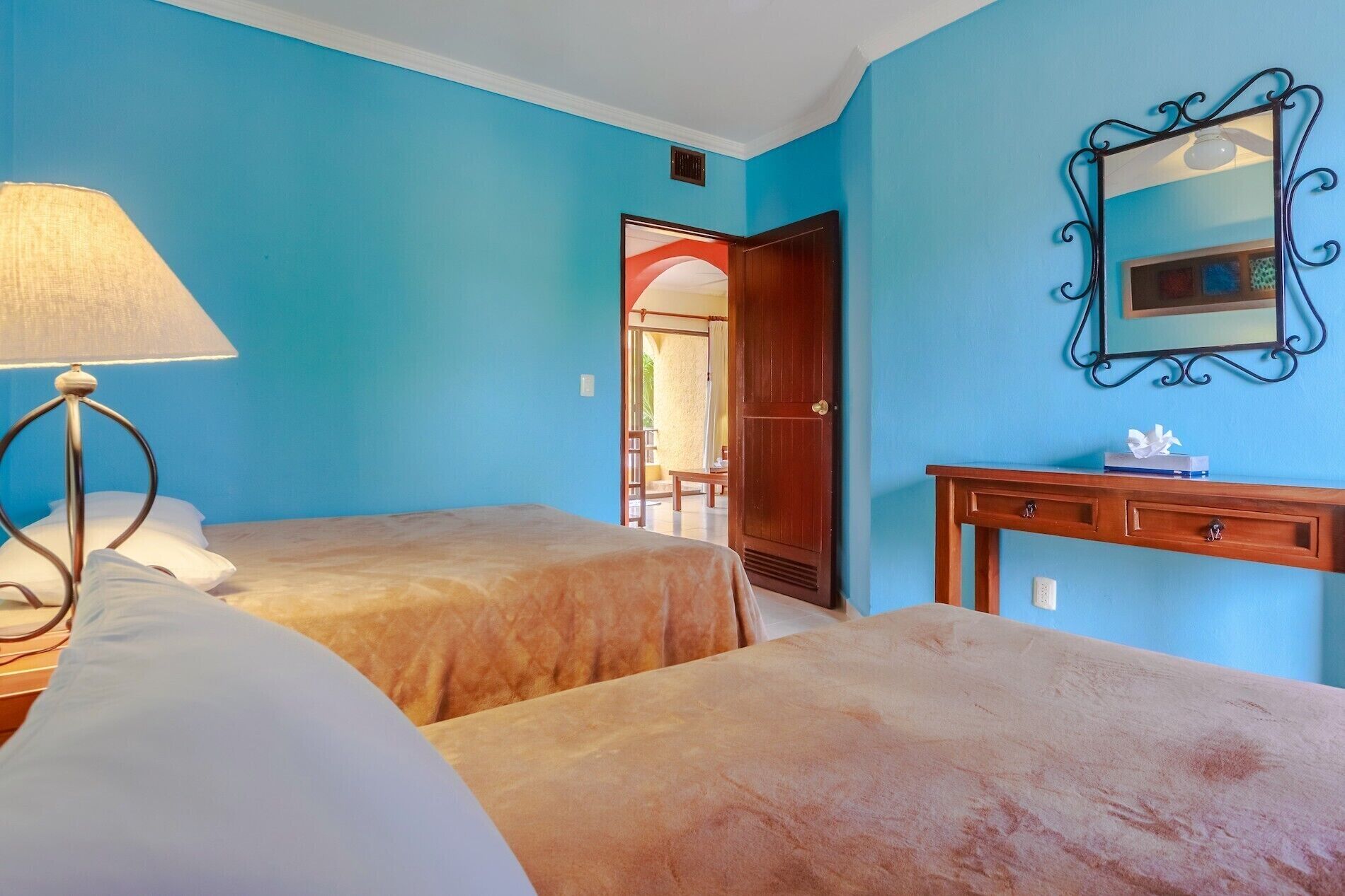 A room with two beds, a desk, a lamp, and a mirror on the wall.