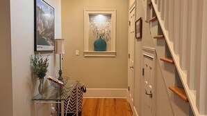 A hallway with wooden flooring, a glass table with a vase and a lamp, a framed picture on the wall, and a staircase with wooden railings. - RELAX, RENEW, REJUVENATE! (Santa Rosa Beach)