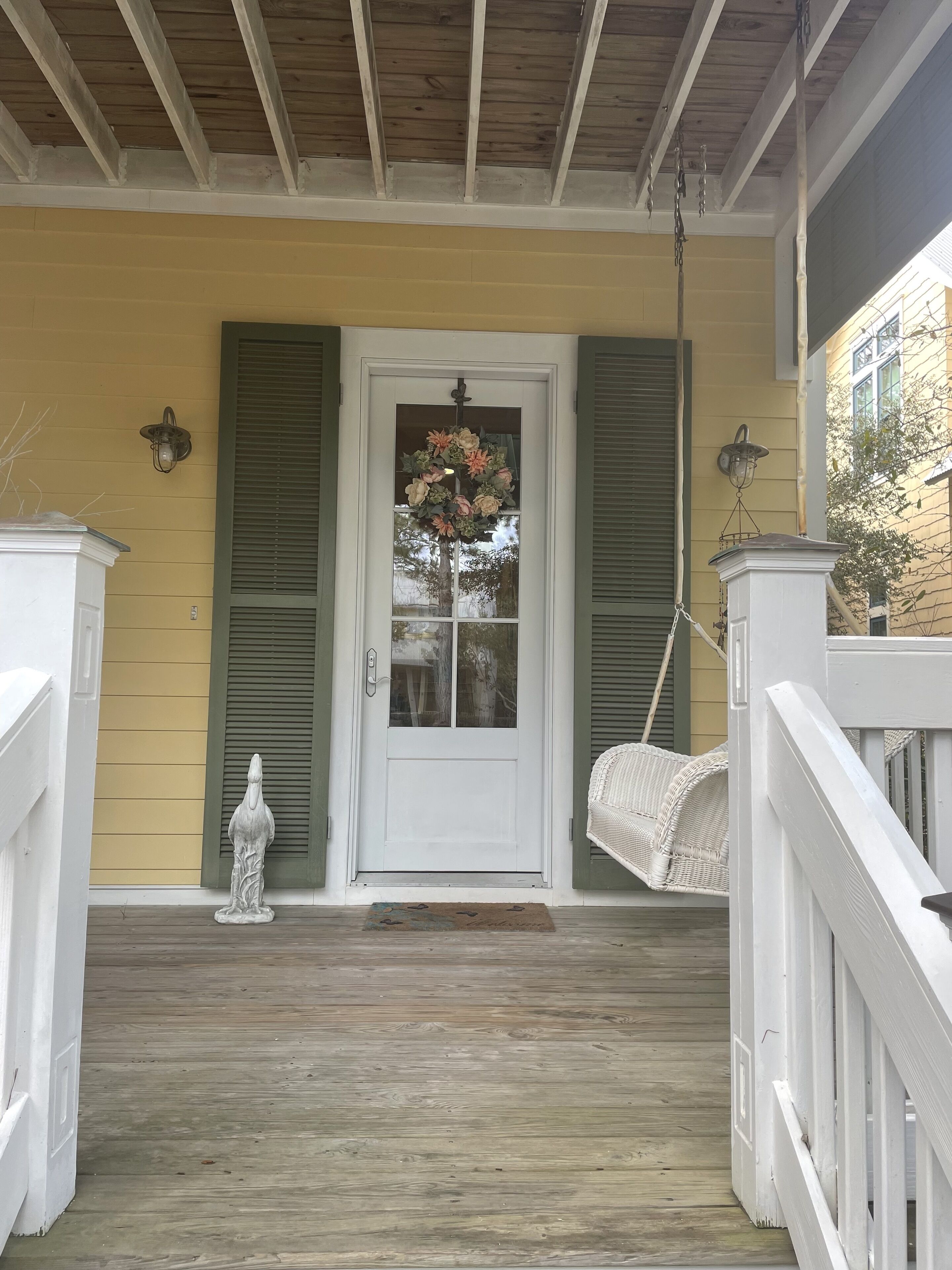 A porch with a white door, green shutters, and a hanging wreath.