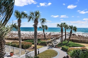 A beachfront property with a wooden deck, palm trees, and a view of the ocean. - Spacious 1BR/1.5BA Beach Condo/Low-Density Complex: Booking for Spring & Summer (Orange Beach)