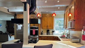 Een moderne keuken met houten kastjes, een roestvrijstalen koelkast, een oven en een koffiezetapparaat. Boven het kookeiland hangen twee hanglampen.