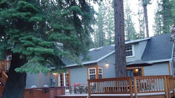 Een chalet met een houten terras, een hottub en een overdekt terras, omringd door bomen.
