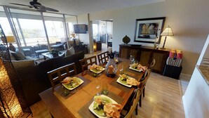 Un comedor con una mesa de madera lista para una comida, un sofá y un televisor al fondo.