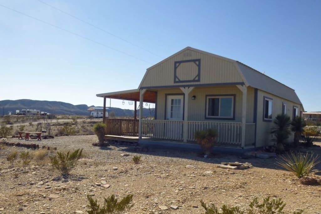 A single-story building with a porch, surrounded by a dry, rocky landscape with sparse vegetation.