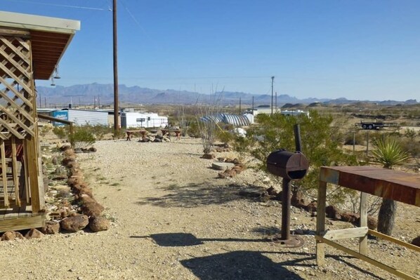A gravel path leading to a building with a wooden lattice structure, a metal grill, and a clear view of mountains in the distance. - Lorna’s Ghost Town Cabin: Located in Ghost Town (Terlingua)
