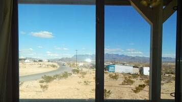 A window view of a desert landscape with a road, buildings, and mountains.