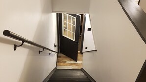 Un escalier avec un plancher en bois et des rampes noires, menant à une pièce dont la porte est dotée d’une fenêtre.