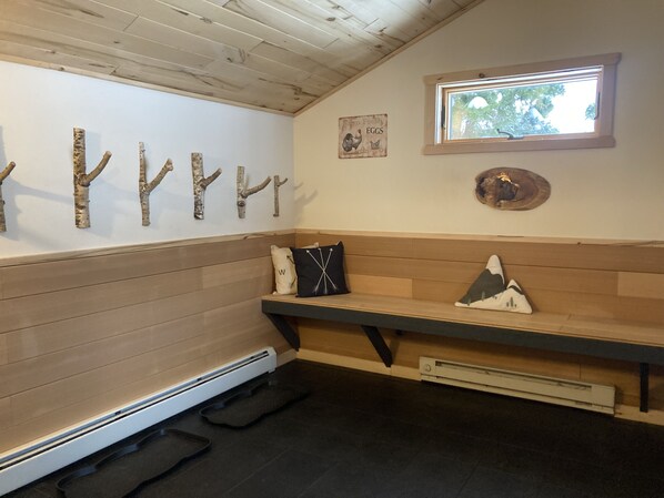 Una habitación con un banco de madera, adornos en la pared y una ventana con vistas a árboles.