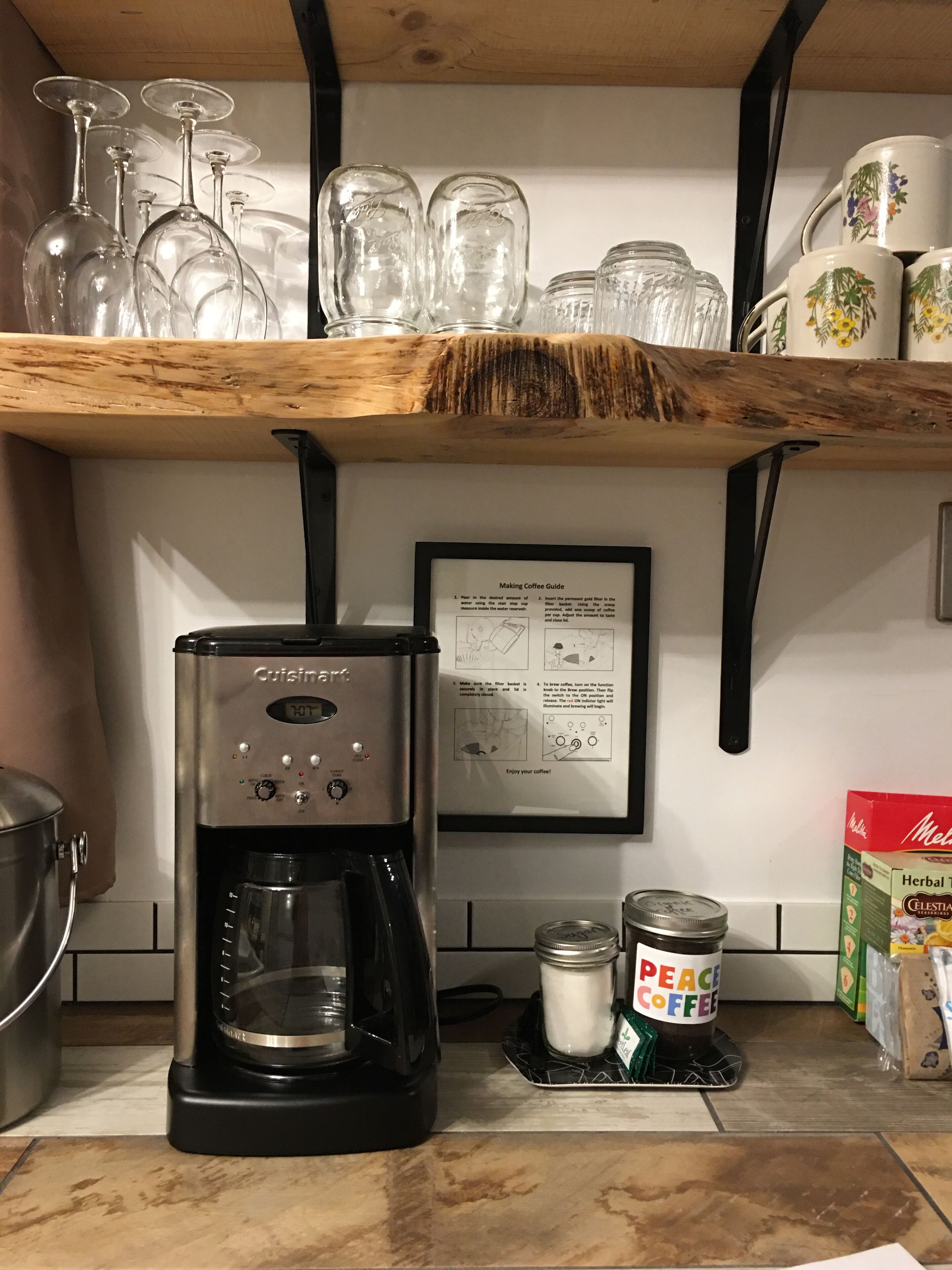 Een keuken met een koffiezetapparaat, een handleiding voor koffie en een plank met drinkglazen en potten.