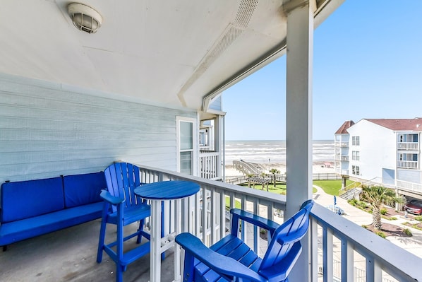 A balcony with blue furniture, a view of the ocean, and a building in the background.