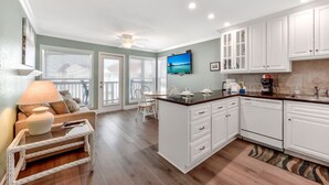 A modern kitchen with white cabinets, a dishwasher, and a dining area with a table and chairs. - AMAZING- beach condo overlooking Pool & Gulf of Mexico 2309 (Galveston)