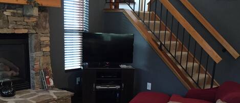 A living room with a stone fireplace, a television, a staircase, and a red couch.