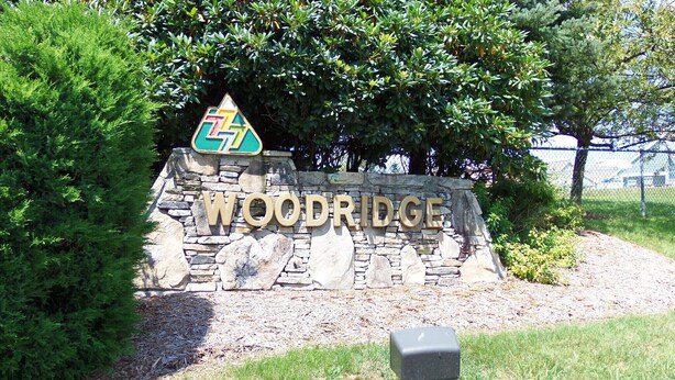A stone sign with "WOODRIDGE" written on it, surrounded by greenery.