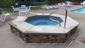 A hot tub with a stone surround, adjacent to a pool with lounge chairs.