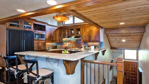 Une cuisine avec des meubles de rangement en bois, un grand îlot central doté de tabourets, et un luminaire suspendu.