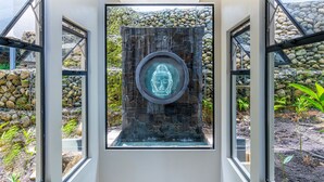 Un intérieur moderne avec une statue de Bouddha au centre, entourée d’un mur de pierre et de panneaux de verre.
