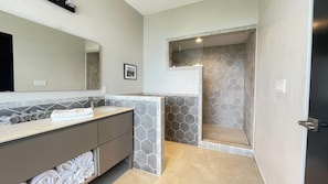A modern bathroom with a large mirror, a vanity with a sink, and a shower area with hexagonal tiles. - Luxury 6BR Ocean-View Villa  Infinity Pool, Spa, Concierge & Full A/C (Uvita)