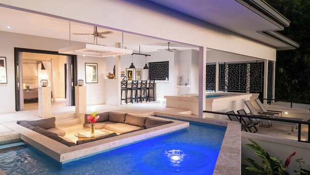 Un espace piscine extérieur moderne, doté d’un coin salon, d’un espace repas et offrant une vue sur le paysage environnant.