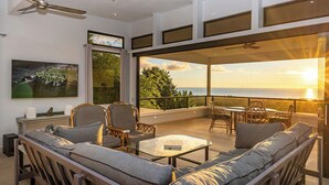 Un salon moderne avec un canapé, des fauteuils et une table, offrant une vue imprenable sur un magnifique coucher de soleil.