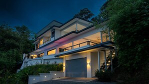 Une maison moderne à deux étages, dotée d’un garage, entourée de verdure et accessible par une allée en gravier.