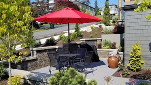 An outdoor patio with a red umbrella, stone steps, and a grill area. - CLASSY, MODERN FAIRHAVEN CONDO WITH GARAGE & EVSE. JUST STEPS TO EVERYTHING! (Bellingham)