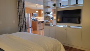 A bedroom with a bed, a TV, and a kitchenette in the background. - CLASSY, MODERN FAIRHAVEN CONDO WITH GARAGE & EVSE. JUST STEPS TO EVERYTHING! (Bellingham)