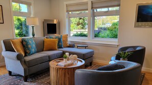A living room with a grey sofa, a round wooden coffee table, and a black armchair. - CLASSY, MODERN FAIRHAVEN CONDO WITH GARAGE & EVSE. JUST STEPS TO EVERYTHING! (Bellingham)