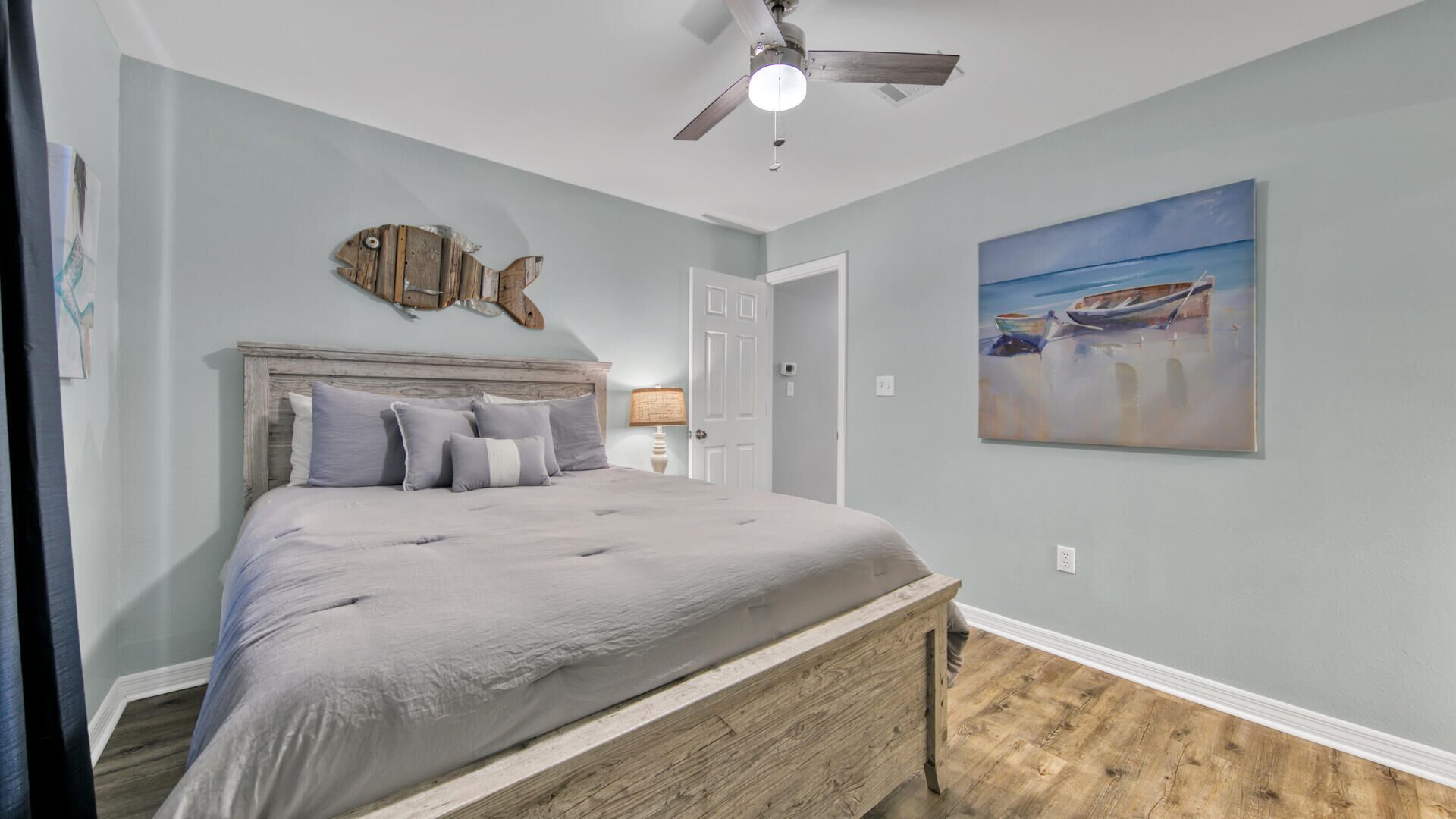 Une chambre avec un lit, un ventilateur de plafond, une décoration murale représentant des poissons et un tableau de bateaux.