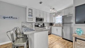 A modern kitchen with white cabinets, stainless steel appliances, and a central island with bar stools. - Beachside Villas - lovely 2BR/2BA unit south of 30A, steps from the beach! (Seagrove Beach)