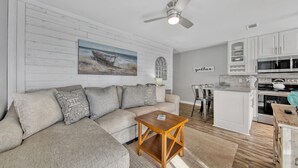 A modern kitchen with white cabinets, a dining area with a bar stool, and a living room with a sofa and a coffee table. - Beachside Villas - lovely 2BR/2BA unit south of 30A, steps from the beach! (Seagrove Beach)