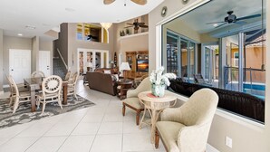 A spacious living area with a dining table, comfortable seating, a large window with a view, and ceiling fans.