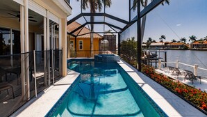 A pool area with a view of a body of water, a covered patio, and a building with a tiled roof.