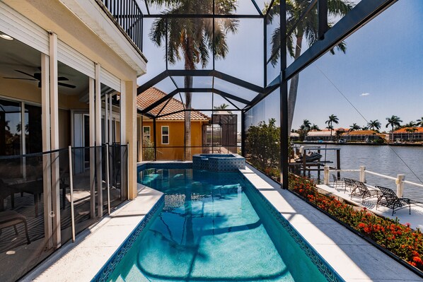 Zona de piscina con vista a una masa de agua, un porche cubierto y un edificio con tejado de baldosas.