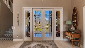 A spacious entrance with a patterned rug, a wooden console table with decorative items, and a staircase on the left.