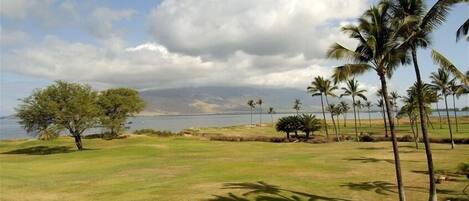 Um campo de golfe com vista para o oceano e montanhas ao fundo.