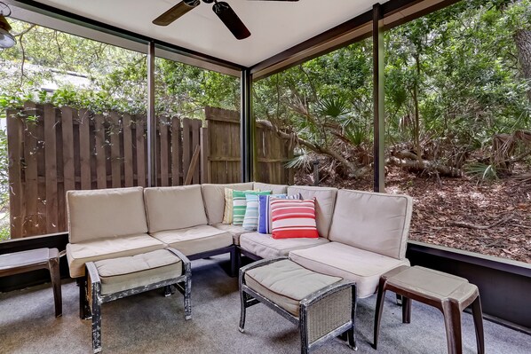 Un área de estar moderna al aire libre con sofá y sillones, ventanas amplias y una valla de madera.