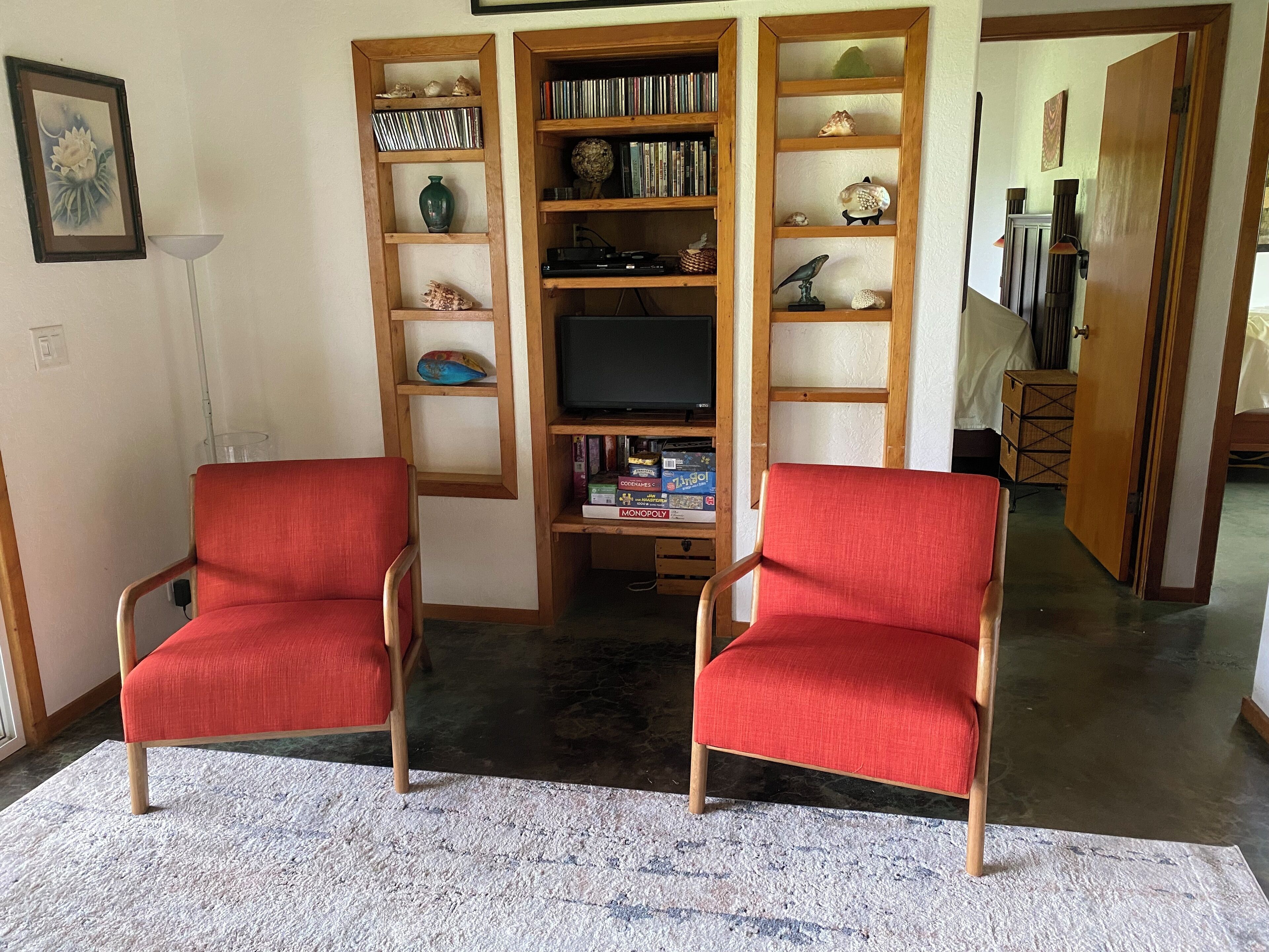 A living room with two red armchairs, a wooden bookshelf, and a flat-screen TV.